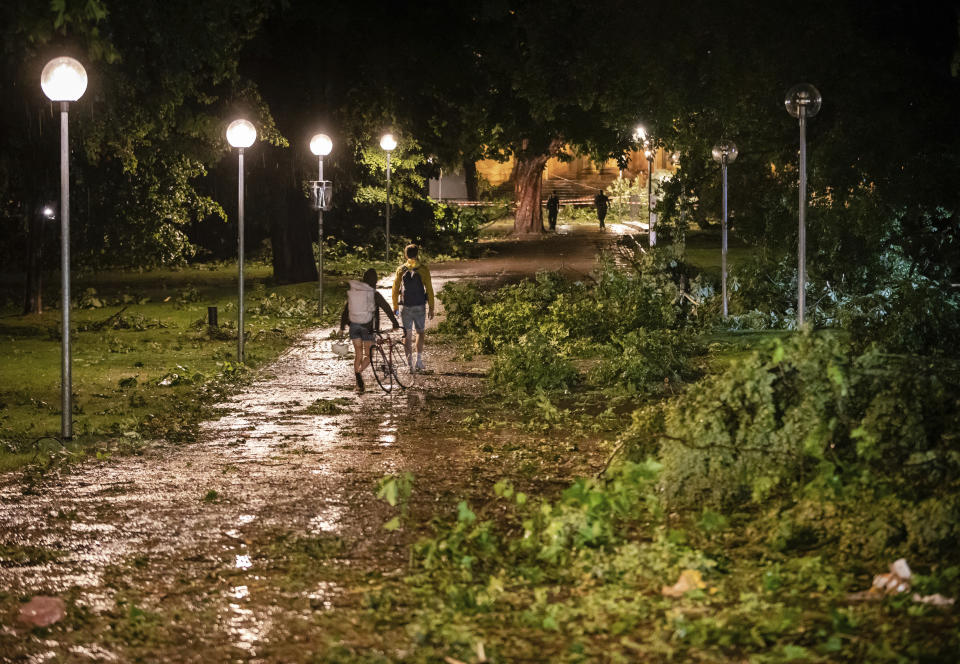 Two persons pass fallen trees at a park in Stuttgart, Germany, Monday, June 28, 2021. Thunderstorms hit Germany late Monday and torrential rains poured down on the southern and western parts of the country leading to dozens of accidents and hundreds of firefighter operations throughout the night. (Christoph Schmidt/dpa via AP)