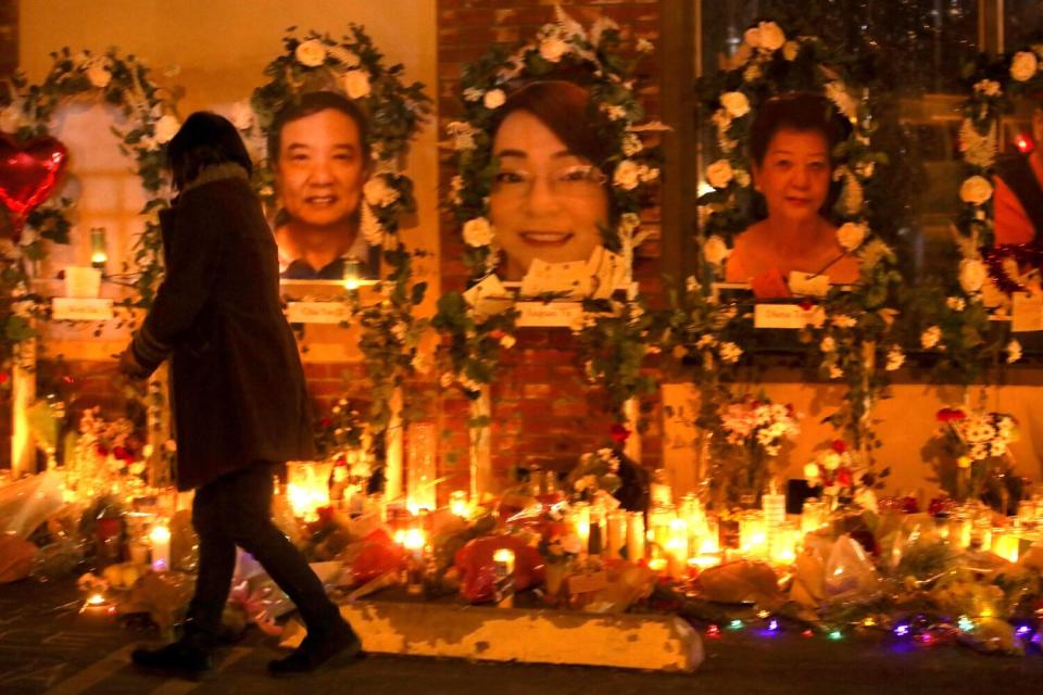 A woman at a memorial with lighted candles and victims' portraits wreathed with flowers