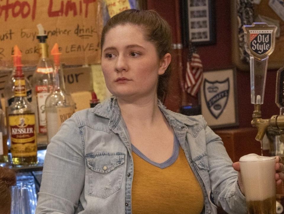 Character Emma Kenney in a denim jacket over a tank top, at a bar with a beer in "Shameless."