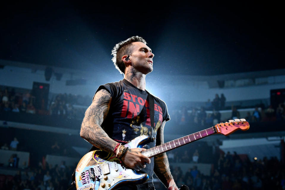Adam onstage, holding an electric guitar and looking out into the crowd, a spotlight shines behind him