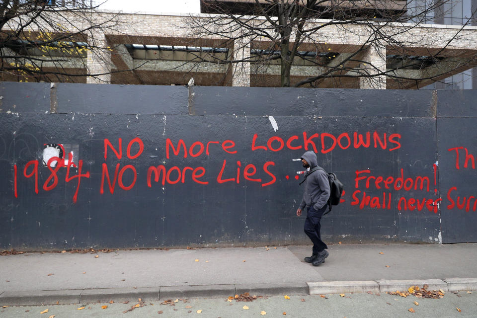 A man walks past anti-lockdown graffiti in Manchester, England, Monday, Oct. 19, 2020 as the row over Greater Manchester region's coronavirus status continues. Britain’s government says discussions about implementing stricter restrictions in Greater Manchester must be completed Monday because the public health threat caused by rising COVID-19 infections is serious and getting worse. (Peter Byrne/PA via AP)