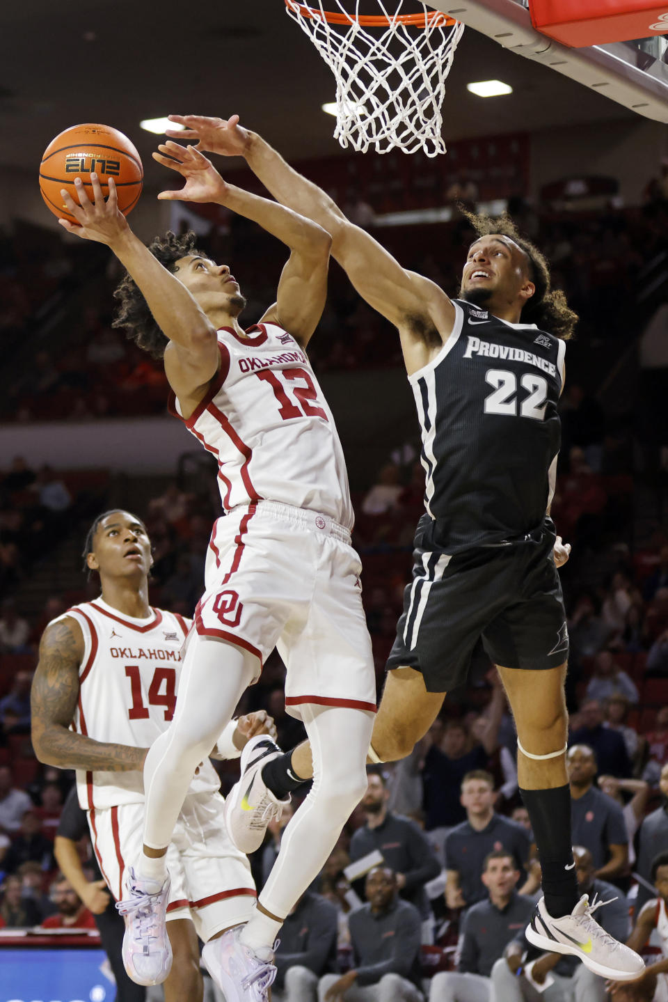 Oklahoma guard Milos Uzan (12) shoots against Providence guard Devin Carter (22) as Oklahoma forward Jalon Moore (14) looks on during the second half of an NCAA college basketball game, Tuesday, Dec. 5, 2023, in Norman, Okla. (AP Photo/Nate Billings)