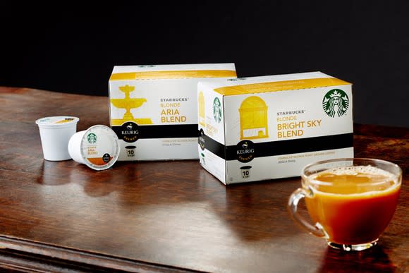 Two boxes of Starbucks K-Cups on a table, along with two K-Cup pods and a cup of coffee