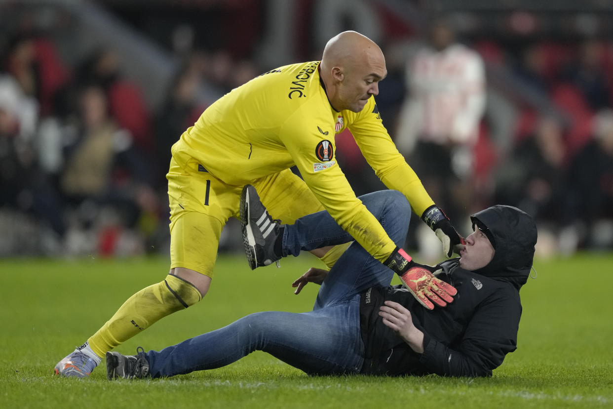 Sevilla's goalkeeper Marko Dmitrovic, top, pushes back a PSV supporter after being punched in the face during the Europa League playoff second leg soccer match between PSV and Sevilla at the Philips stadium in Eindhoven, Netherlands, Thursday, Feb. 23, 2023. Sevilla won 3-2 on aggregate. (AP Photo/Peter Dejong)