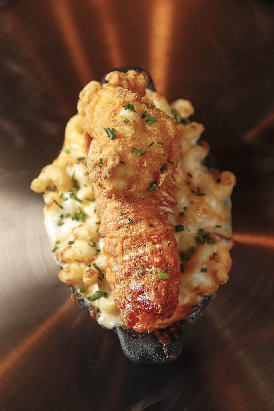 A skillet dish of mac and cheese topped with a piece of fried chicken, garnished with green herbs