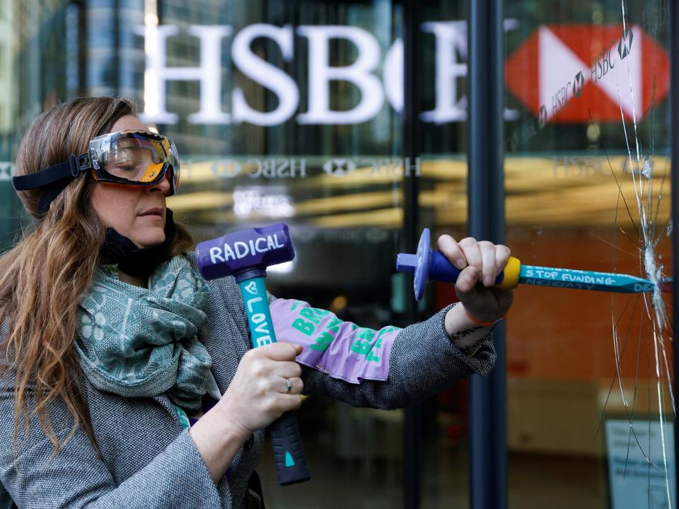 An activist from the Extinction Rebellion shatters a window at HSBC headquarters in Canary Wharf (Reuters)