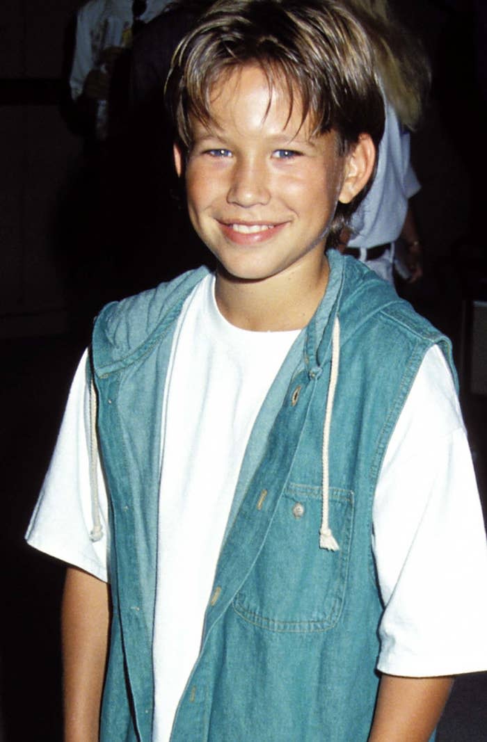 A young Jonathan Taylor Thomas smiles while wearing a denim vest, looking very '90s