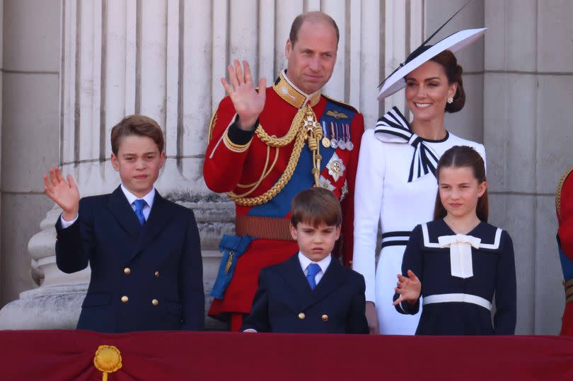 Kate smiles as William waves and they appear on the balcony with their children