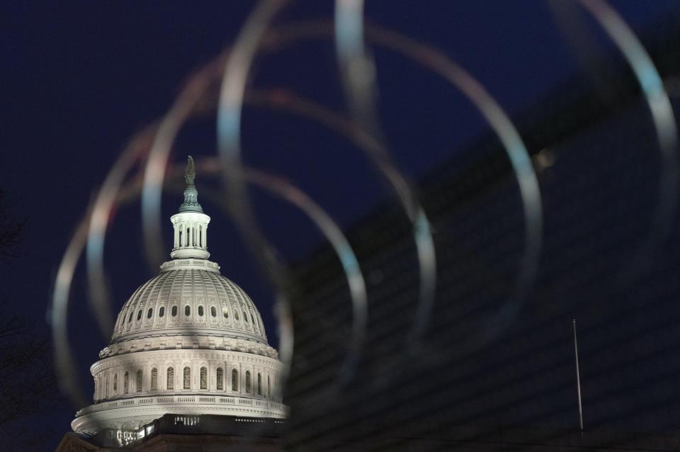 Le dôme du Capitole américain est visible dans l’obscurité derrière les barbelés