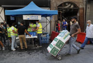 A man carries donated food as he passes in front of a tent that citizens set up to offer people food and drinks, on a street that was damaged by last week's explosion, in Beirut, Lebanon, Tuesday, Aug. 11, 2020. In the absence of the state, acts of kindness and solidarity have been numerous and striking. Many extended a helping hand far beyond their circle of friends or family, taking to social media to spread the word that they have a room to host people free of charge. (AP Photo/Hussein Malla)