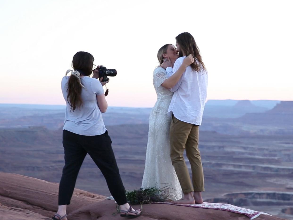 a wedding photographer getting a shot of the bride and groom standing in front of a vast landscape