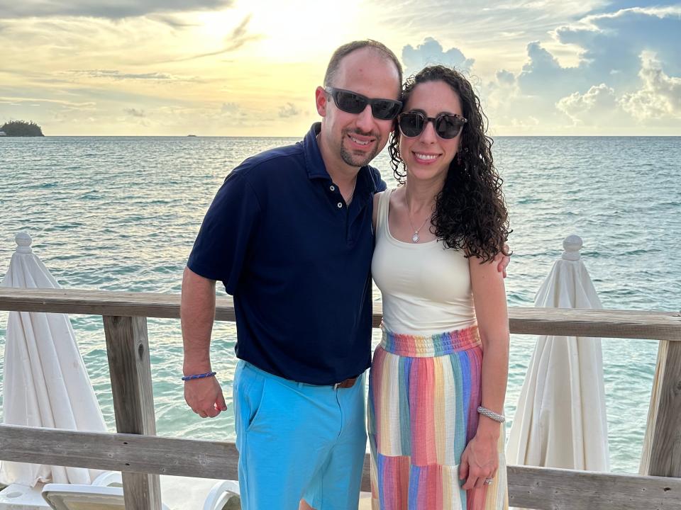 Lindsay Karp and her husband wearing sunglasses while on vacation with the ocean and sunset in the background.