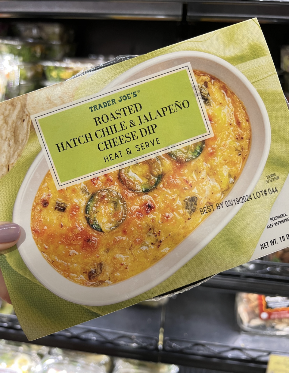 Hand holding a package of Trader Joe's Roasted Hatch Chile & Jalapeño Cheese Dip in a grocery store