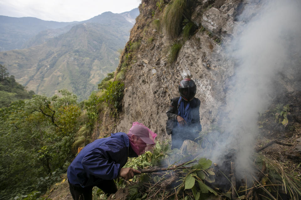 Honey hunters make a fire to distract bees from hives before they harvest the cliff honey in Dolakha, 115 miles east of Kathmandu, Nepal, Nov. 19, 2021. High up in Nepal's mountains, groups of men risk their lives to harvest much-sought-after wild honey from hives on cliffs. (AP Photo/Niranjan Shrestha)