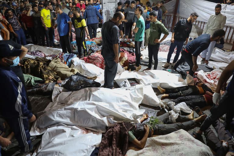 Personas se reúnen alrededor de los cuerpos de palestinos fallecidos en los ataques aéreos israelíes en el hospital Ahli Arab en el centro de Gaza después de ser trasladados al hospital Al-Shifa, el 17 de octubre de 2023.