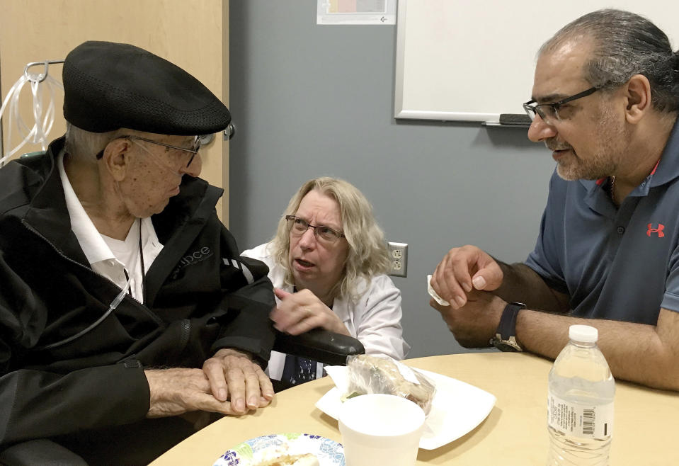 The Rev. John Sabbagh, left, and his son Ebby Sabbagh talk with nurse practitioner Kim O'Riley, Friday, Sept. 7, 2018 in Gilbert, Ariz. Thirty-five years after John Sabbagh cared for his son when he was shot in their native Lebanon, Ebby is returning that devotion. Both the Rev. John Ibraham Sabbagh and 54-year-old son, Ebby Sabbagh, are celebrating one year of going strong since the elder Sabbagh received a crucial stem-cell transplant. (AP Photo/Terry Tang)