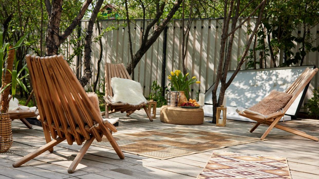 wooden easy chairs with pillows and carpets placed near green trees in daylight