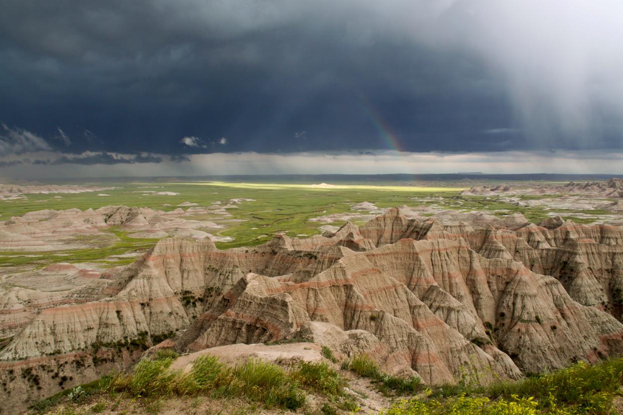 A rainbow is seen among dark clouds over Badlands National Park.