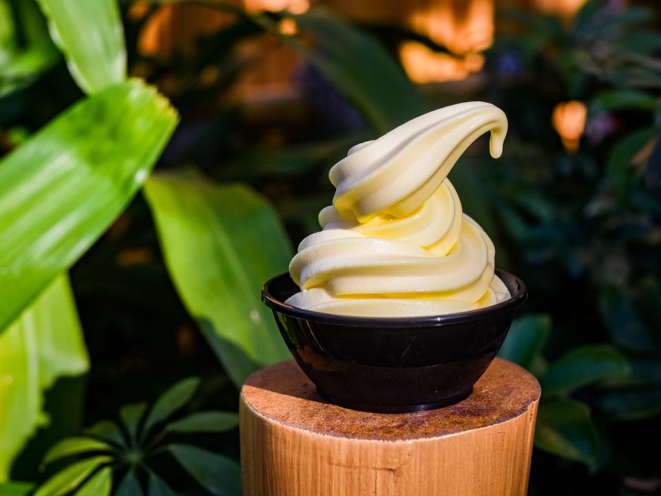 cup of dole whip resting on a pillar at disneyland  with greenery in the background
