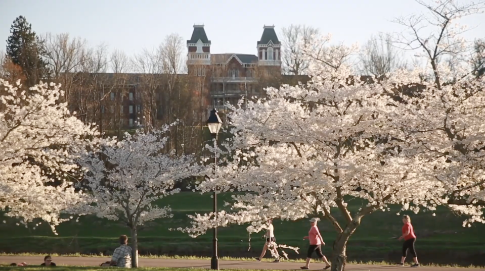 a group of people running on a grass field with trees and a building in the background