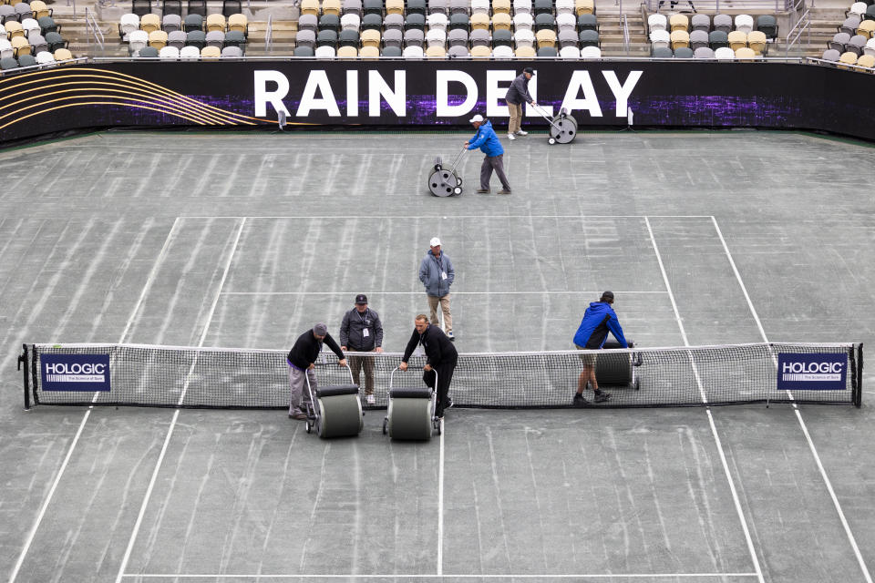 Officials work to dry the court after a rain delay was called during the semifinal match between Daria Kasatkina, of Russia, and Ons Jabeur, of Tunisia, at the Charleston Open tennis tournament in Charleston, S.C., Saturday, April 8, 2023. (AP Photo/Mic Smith)