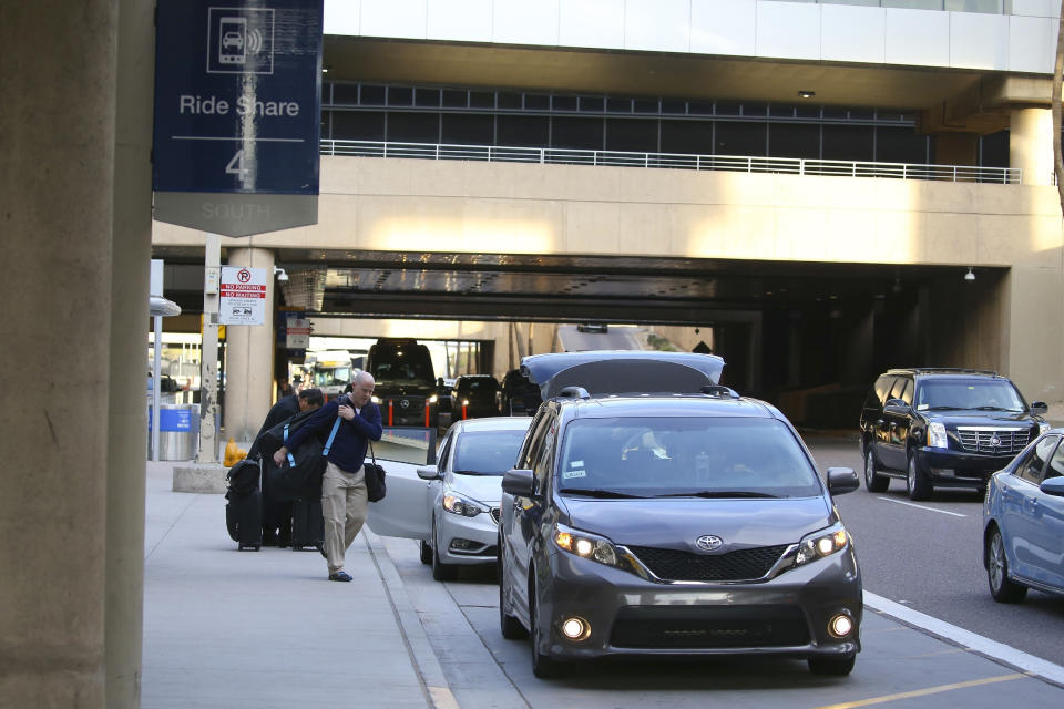 FILE - In this Dec. 18, 2019, file photo passengers find their rides at the Ride Share point as they exit Phoenix Sky Harbor International Airport in Phoenix. The Arizona Supreme Court has unanimously ruled that the Phoenix airport can raise fees for Uber and Lyft to pick up and drop off customers. The ride-hailing companies have threatened to stop serving the airport over the $4 pickup and drop-off fees. The court on Thursday, April 2, 2020 rejected a complaint filed by Republican Attorney General Mark Brnovich, who said the fee hikes are "very likely" unconstitutional. (AP Photo/Ross D. Franklin, File)