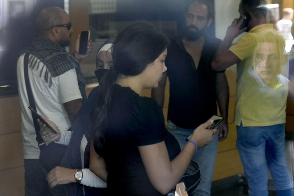 A man's face is reflected on a window as Lebanese Sali Hafez, center, accompanied by activists looks at her phone after breaking into a BLOM Bank branch brandishing what she later said was a toy pistol and taking $13,000 from her trapped savings account, in Beirut, Lebanon, Wednesday, Sept. 14, 2022. Lebanon's cash-strapped banks have imposed strict limits on withdrawals of foreign currency since 2019, tying up the savings of millions of people. About three-quarters of the population has slipped into poverty as the tiny Mediterranean country's economy continues to spiral. (AP Photo/Hussein Malla)