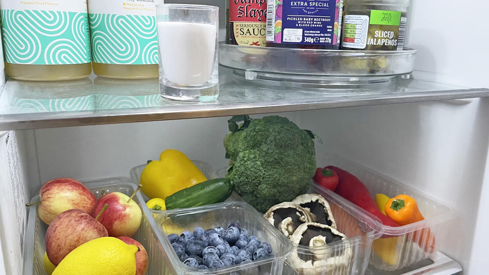 fridge with vegetables and glass container of baking soda on upper shelf