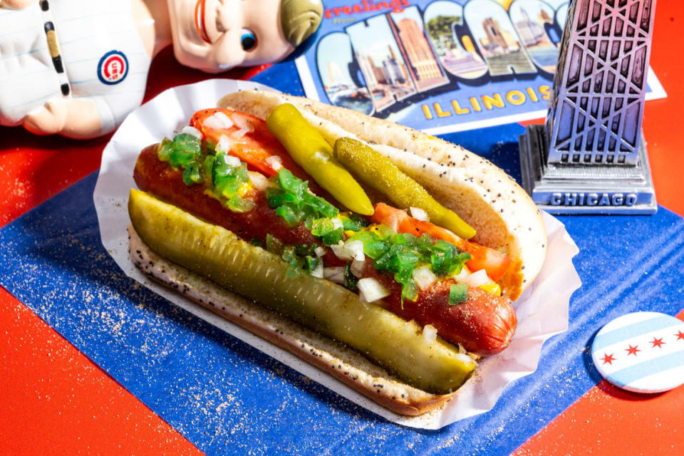 A hot dog with pickles against a backdrop of Chicago memorabilia, including a Cobs bobblehead