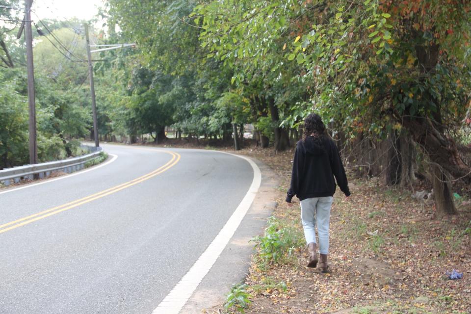 A woman walks on the side of a wooded road.
