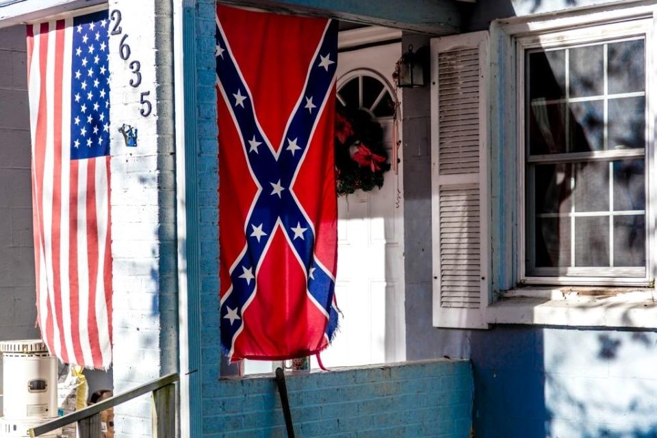 An American flag and a Confederate flag hang side by side on a house's front porch