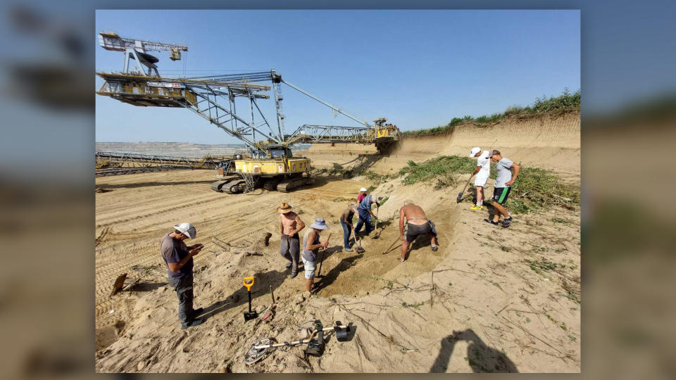 We see a crane and people excavating a desert-like site on a hill.