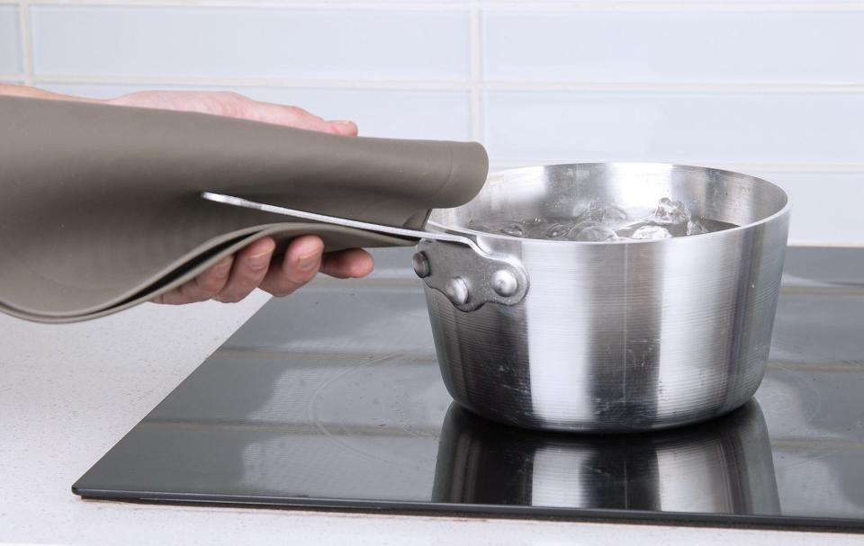 Person using the mat as a potholder to hold a pot handle on a stove