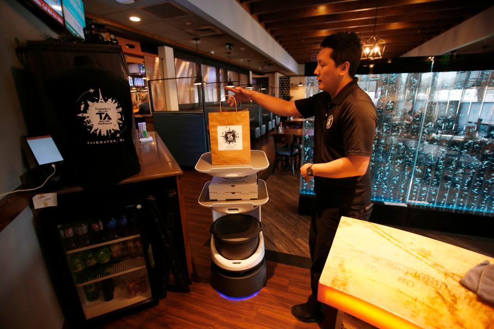 Traveler's Alehouse owner Minh Tieu removes the sample food items from the top of the robot after it successfully delivered them to the front desk of the Fairhaven restaurant. The robot which staff call Wall-E, gives staff a hand in bringing orders for take-out and to the tables.