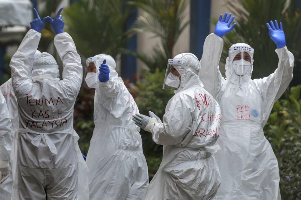 Health workers wave to members of the media at Menara City One in Kuala Lumpur April 14, 2020. — Picture by Ahmad Zamzahuri