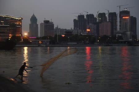 A man casts a net by the side of a river next to a construction site of new residential buildings in Wuhan, Hubei province, July 31, 2014. REUTERS/Stringer