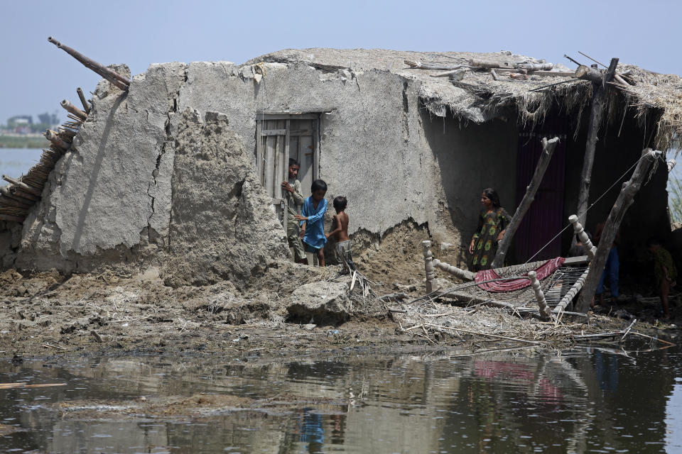 Children stand in front of their flooded home after monsoon rains, in the Qambar Shahdadkot district of Sindh Province, of Pakistan, Tuesday, Sept. 6, 2022. More than 1,300 people have been killed and millions have lost their homes in flooding caused by unusually heavy monsoon rains in Pakistan this year that many experts have blamed on climate change. (AP Photo/Fareed Khan)