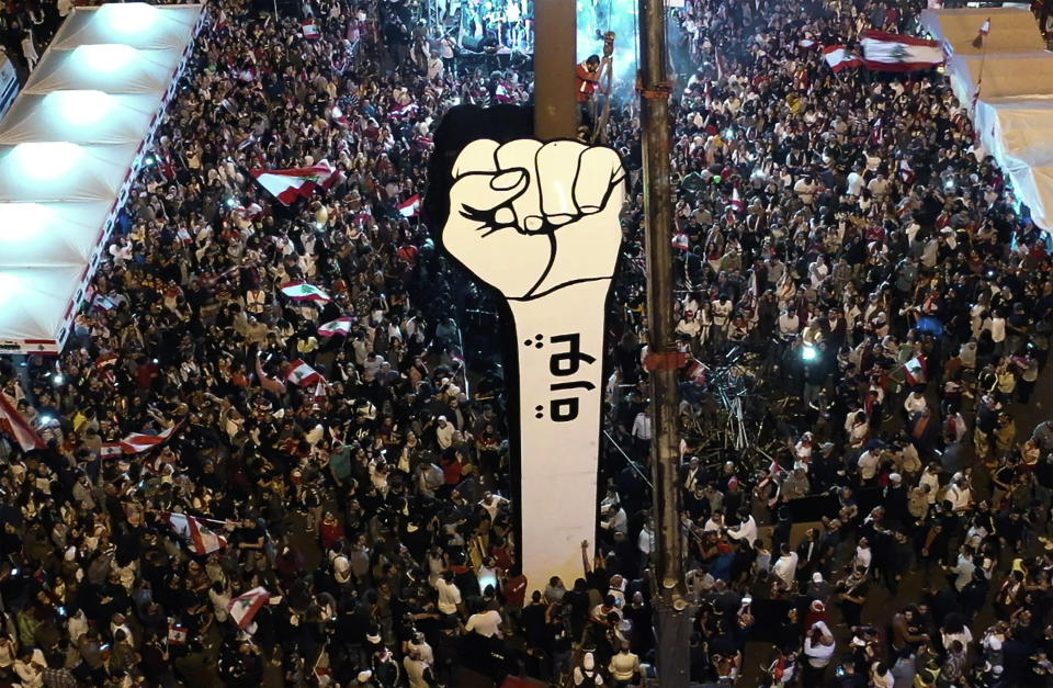 In this photo from a drone, anti-government protesters re-install a new large cardboard fist labelled "Revolution" in Martyr's Square after a previous one was burned down overnight by unknown vandals, at the Martyr square, in downtown Beirut, Lebanon, Friday, Nov. 22, 2019. Lebanon's protesters and top politicians held competing Independence Day celebrations Friday, reflecting the deepening rift that has beset the country grappling with its worst political and economic crises in decades. (AP Photo/Hussein Malla)