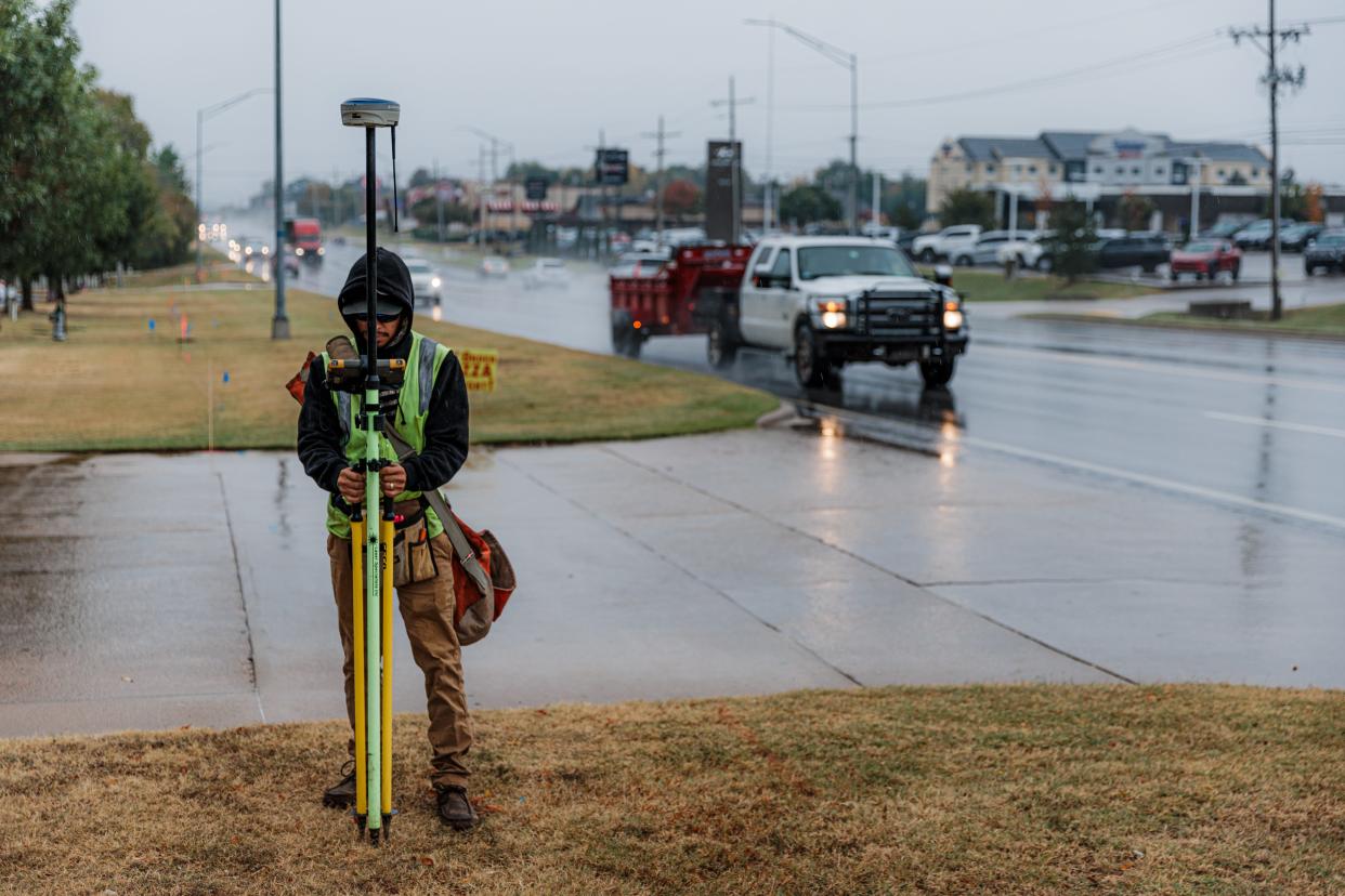 An ODOT surveyor works in the rain Tuesday to mark out where new sidewalks will be along U.S. Highway 75 in Bartlesville.
