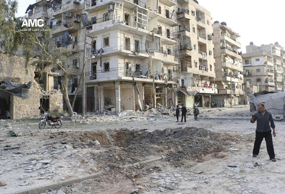 In this photo taken on Thursday April 24, 2014, and provided by the anti-government activist group Aleppo Media Center (AMC), which has been authenticated based on its contents and other AP reporting, shows Syrian man, right, takes pictures with his mobile phone of a crater from a government forces airstrike, in Aleppo, Syria. Syrian government airstrikes struck a vegetable market in a northern rebel-held town Thursday, killing dosens of people and wounding scores of others, an activist group said. (AP Photo/Aleppo Media Center, AMC)