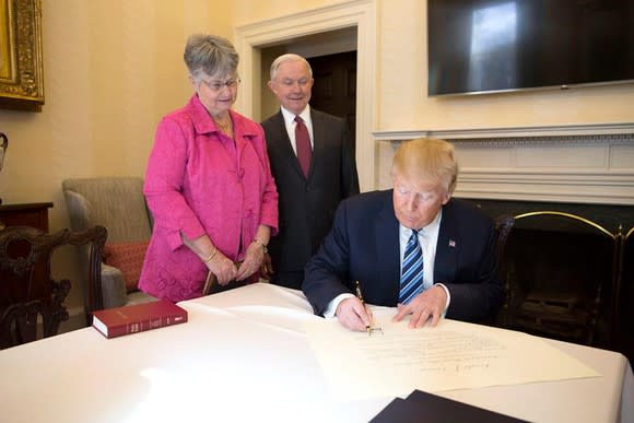 President Trump signing paperwork, with Attorney General Jeff Sessions and his wife to his right.