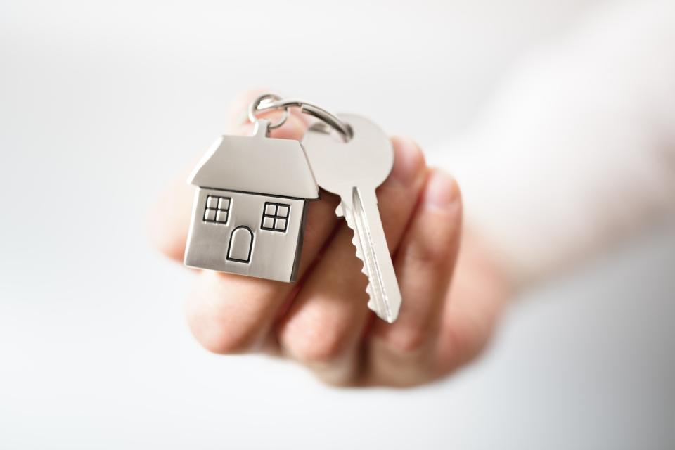 Hand holding keys and a miniature house, all on a key ring