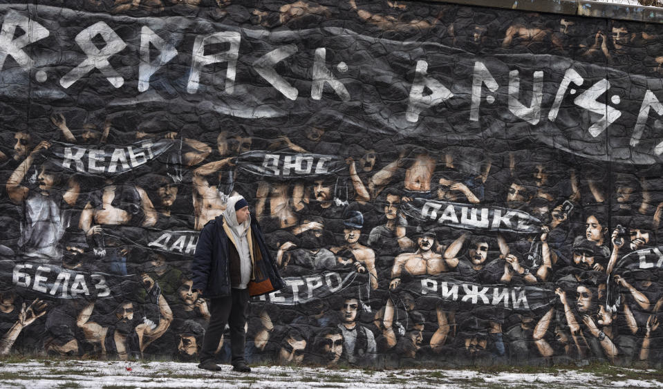 Un hombre pasa junto a un mural inspirado en una fotografía tomada en febrero de 2023 en un partido de fútbol entre el Dinamo de Zagreb y el Hajduk de Split en Zagreb, en un muro de contención en Kiev, Ucrania, el 19 de enero de 2024. Los aficionados del Dinamo homenajearon a los soldados ucranianos fanáticos del deporte muertos en combate frente a las tropas rusas, y mostraron carteles con sus nombres y la frase "Gloria a Ucrania" en el primer aniversario de la invasión rusa. La pancarta más grande pone "División Borodach", una unidad del Regimiento de Azov formada por aficionados al fútbol. (AP Foto/Efrem Lukatsky)