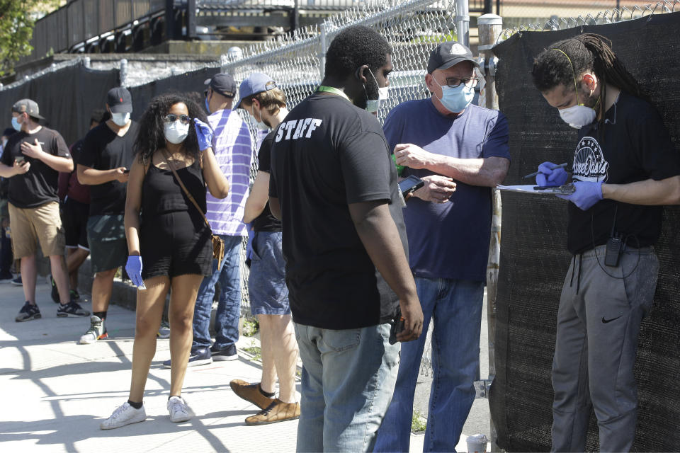 Employees of Pure Oasis recreational marijuana store, third from right and right, assist a patron standing in line outside the store, Tuesday, May 26, 2020, in Boston. Sales of recreational cannabis products to the public was allowed to open Monday, May 25 in Massachusetts after being closed for about two months due to the coronavirus pandemic. (AP Photo/Steven Senne)
