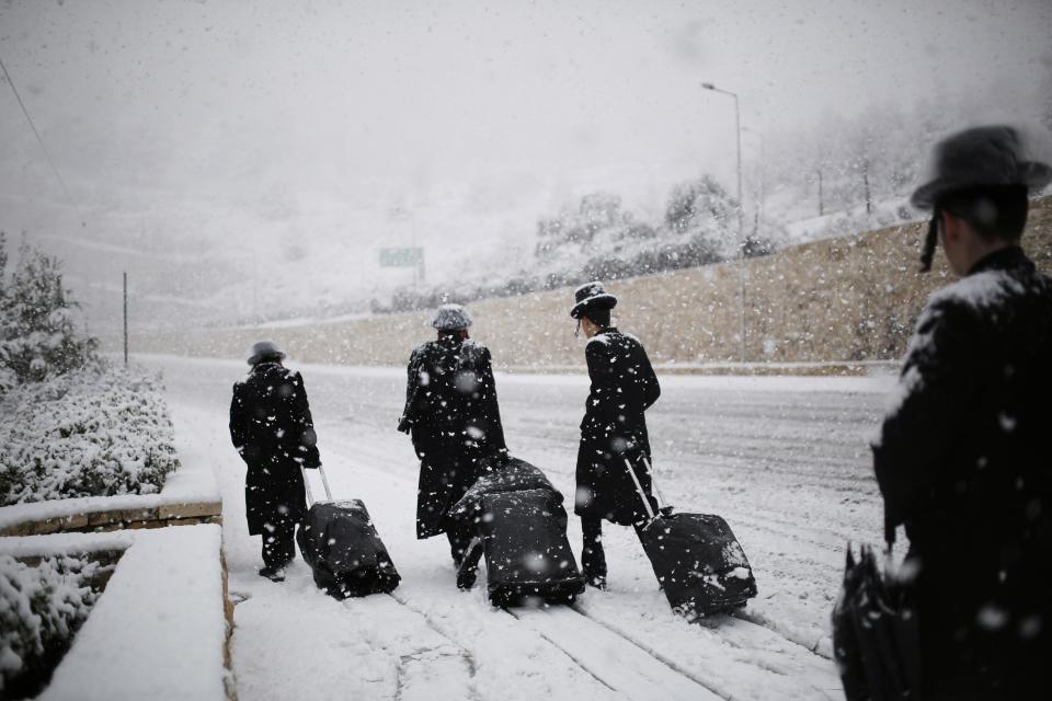 Ultra-Orthodox Jewish men walk on a snow-covered road in winter in Jerusalem