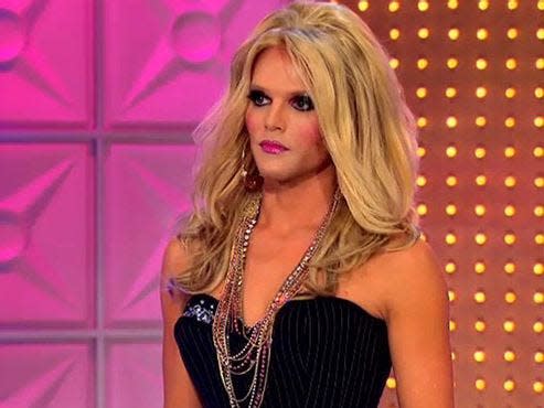 Willam in a black dress and blonde wing on drag race stage