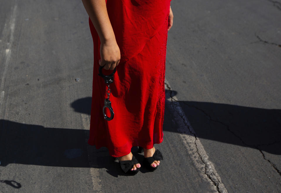 A demonstrator wears a red dress as she holds a pair of handcuffs during the International Women's Day strike "A Day Without Women" at Zocalo square in Mexico City, Monday, March 9, 2020. Thousands of women across Mexico went on strike after an unprecedented number of girls and women hit the streets to protest rampant gender violence on International Women's Day. (AP Photo/Fernando Llano)