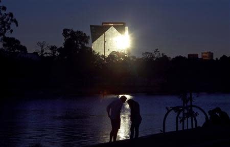 A man and a woman stand on the banks of Melbourne's Yarra River as a building reflects the setting sun behind them in this January 16, 2013 file photo. REUTERS/David Gray/Files