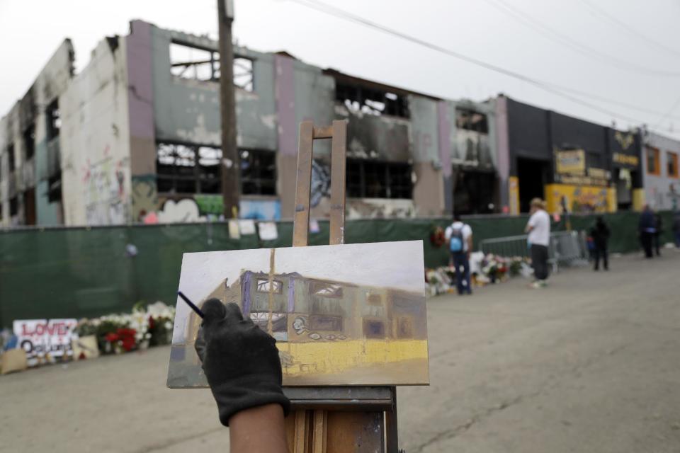 Artist John Paul Marcelo paints the scene of a warehouse fire Tuesday, Dec. 13, 2016, in Oakland , Calif. The fire killed dozens of people during a electronic dance party as it raced through the building, in the deadliest structure fire in the U.S. in more than a decade. (AP Photo/Marcio Jose Sanchez)