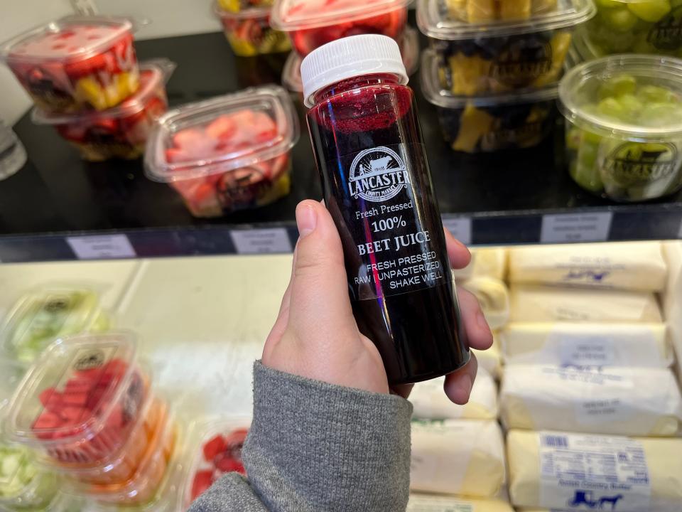 A bottle of 100% beet juice held by a hand wearing a grey sweatshirt